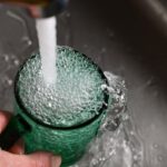 Tap Water - a person's hand is holding a green cup with water coming out of it