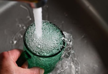 Tap Water - a person's hand is holding a green cup with water coming out of it