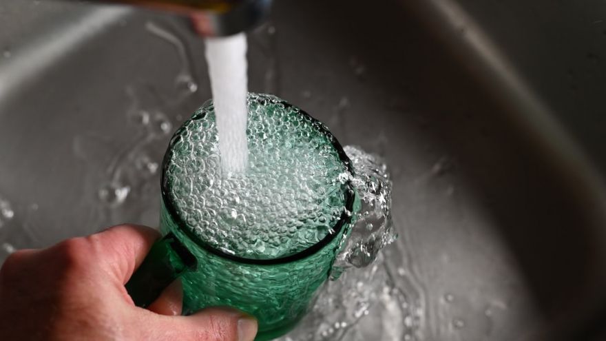 Tap Water - a person's hand is holding a green cup with water coming out of it