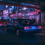 Japanese Car - people walking on pathway near buildings and different vehicles on road during night time