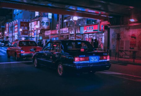 Japanese Car - people walking on pathway near buildings and different vehicles on road during night time