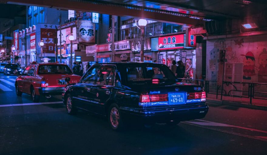 Japanese Car - people walking on pathway near buildings and different vehicles on road during night time