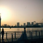 Japan Romantic - a couple of people standing on a bridge over water with a city in the background