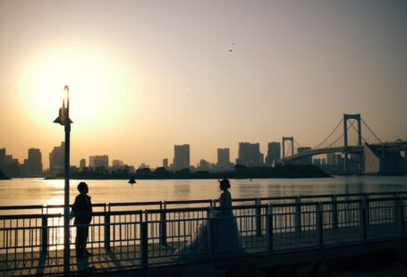 Japan Romantic - a couple of people standing on a bridge over water with a city in the background