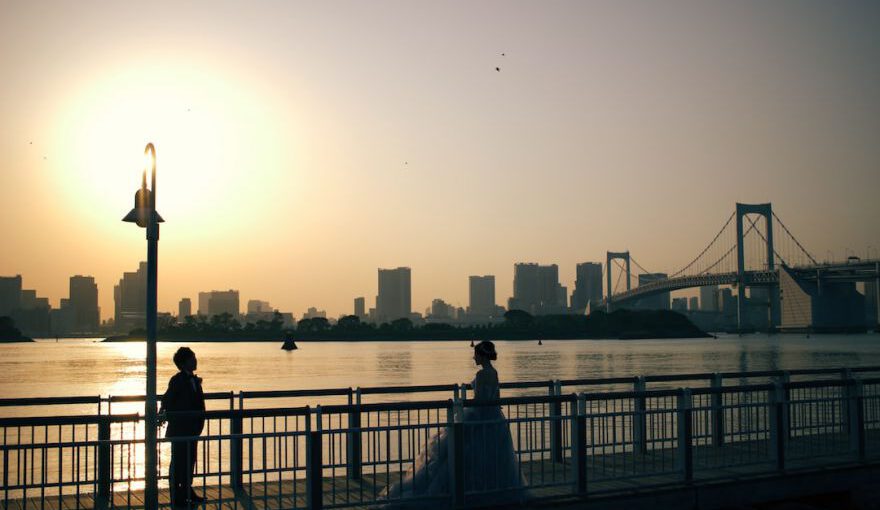 Japan Romantic - a couple of people standing on a bridge over water with a city in the background