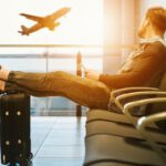 Safe Travel - man sitting on gang chair with feet on luggage looking at airplane