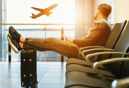 Safe Travel - man sitting on gang chair with feet on luggage looking at airplane