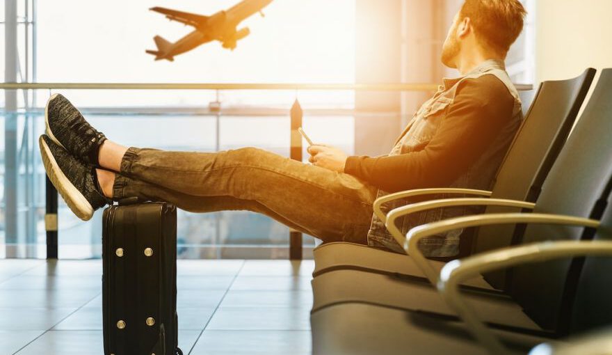 Safe Travel - man sitting on gang chair with feet on luggage looking at airplane